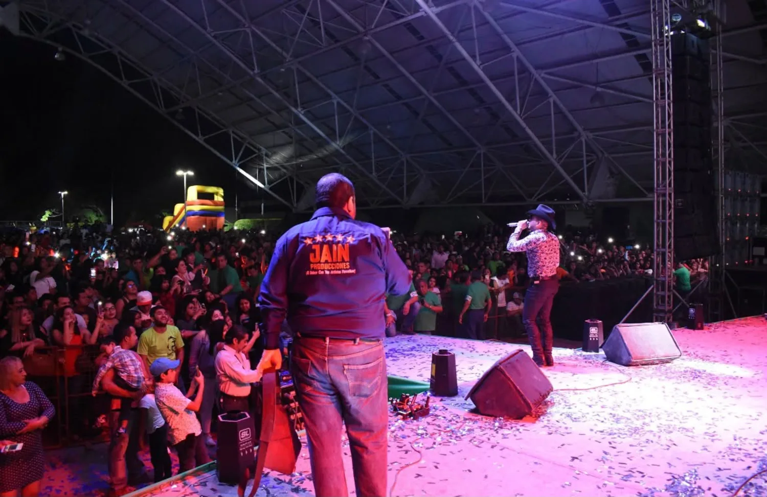 Artista en escenario con equipo de Jain Producciones frente a público